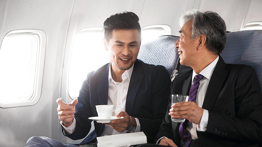 飞机上交谈的商人；图片用于公司雇员专享计划